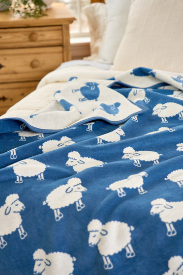 Blue and white reversible blanket with sheep pattern on bed, cream side visible on top fold.2