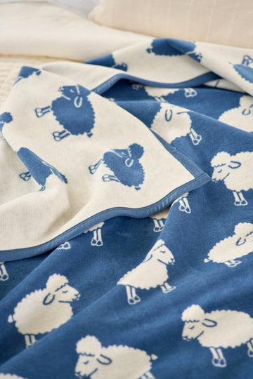 Blue and cream blanket with repeating sheep pattern, shown folded on a light background.3
