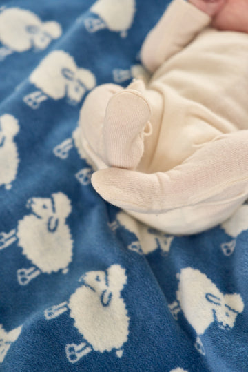 Blue blanket with white lamb print, cream-colored corner with bundled fabric detail visible.3