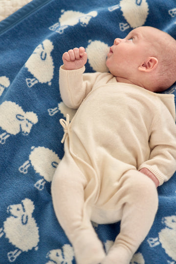 Blue mini blanket with cream sheep pattern, displayed with infant in cream outfit.2