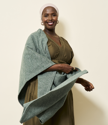 Green herringbone woven shawl draped over olive dress, shown on model against neutral background.3