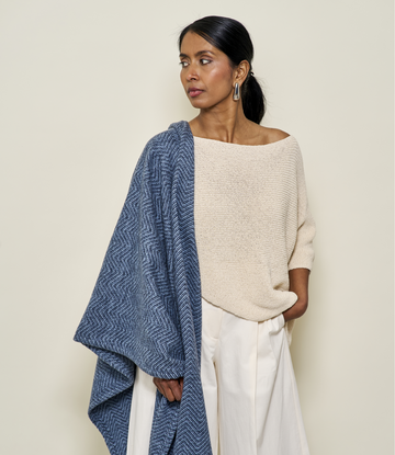 Navy herringbone shawl draped over woman's shoulder, worn with cream sweater and white pants.6
