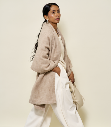 Wheat-colored herringbone shawl with textured weave draped over shoulders, worn with white pants.6