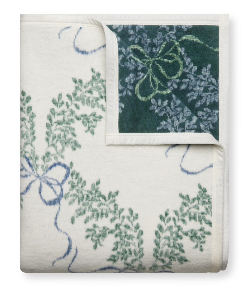 Folded blanket with cream and dark green sides featuring boxwood wreath patterns and blue ribbon designs.