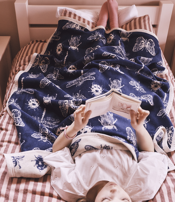 Navy blanket with white insect and bug print draped over child on striped bedding.2