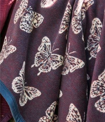 Burgundy blanket with cream and brown butterfly pattern, folded to show texture and design detail.4