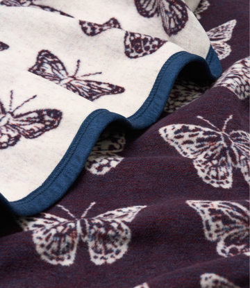 Folded blanket with purple and cream butterfly print on both sides, showing blue binding edge.5