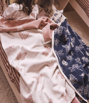 Cream and navy blankets with embroidered butterfly and insect patterns draped over two children on a striped chair.5