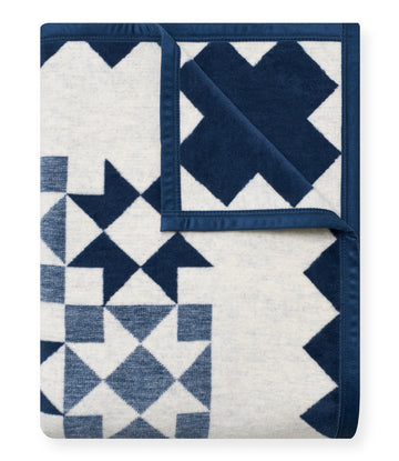 Folded quilt blanket with navy and cream patchwork geometric patterns and navy binding edges.8