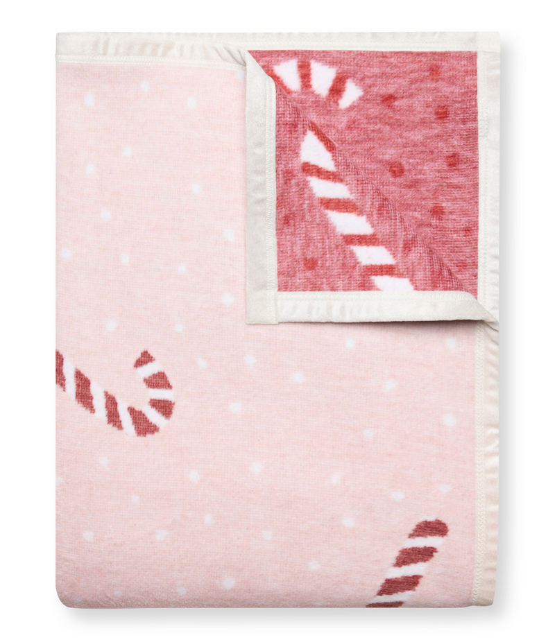 Pink and red knit blanket with candy cane stripes and white polka dots, folded with white binding edges.