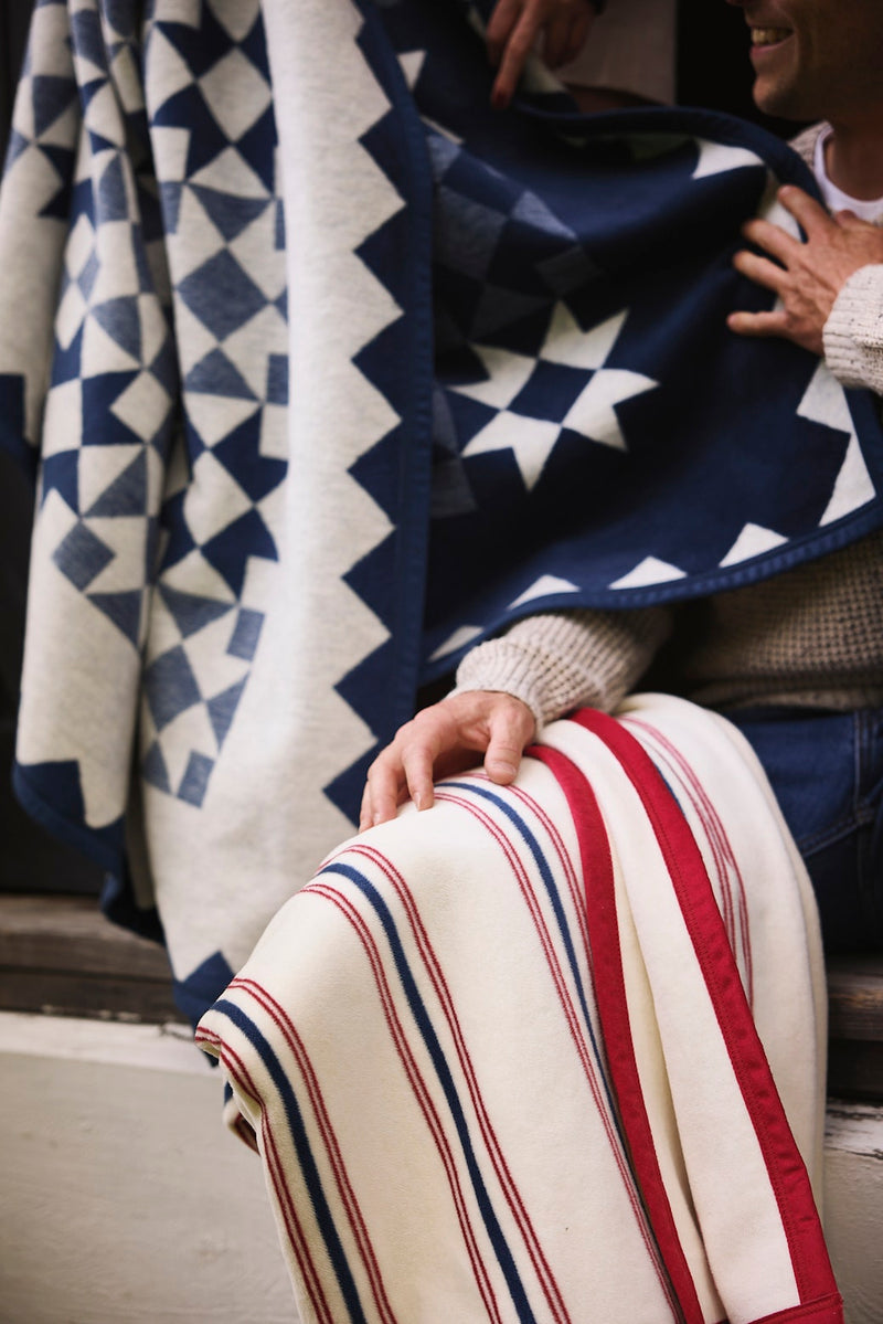 Navy and cream blanket with geometric star and diamond pattern, displayed draped over a person's lap with red and navy stripe