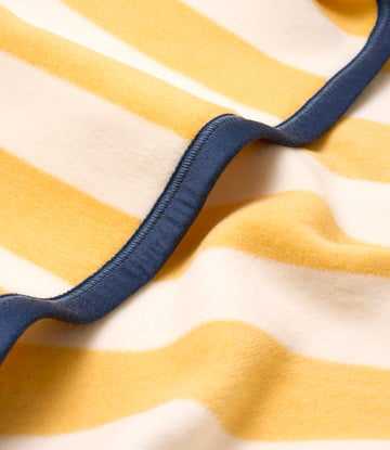 Striped blanket with yellow and cream horizontal stripes and navy blue binding along the edge.7