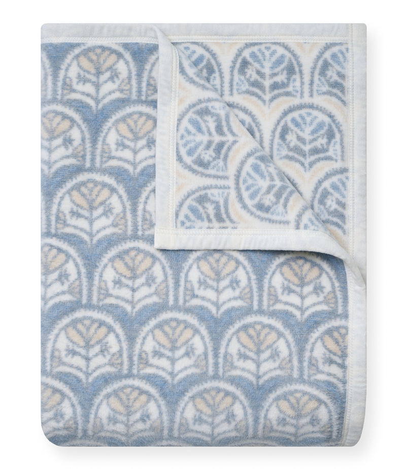 Folded blanket with blue and cream scallop shell pattern and white trim.