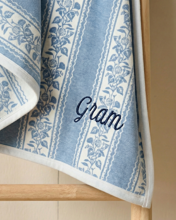 Blue and white patterned blanket with 'Gram' embroidery on a wooden rack.