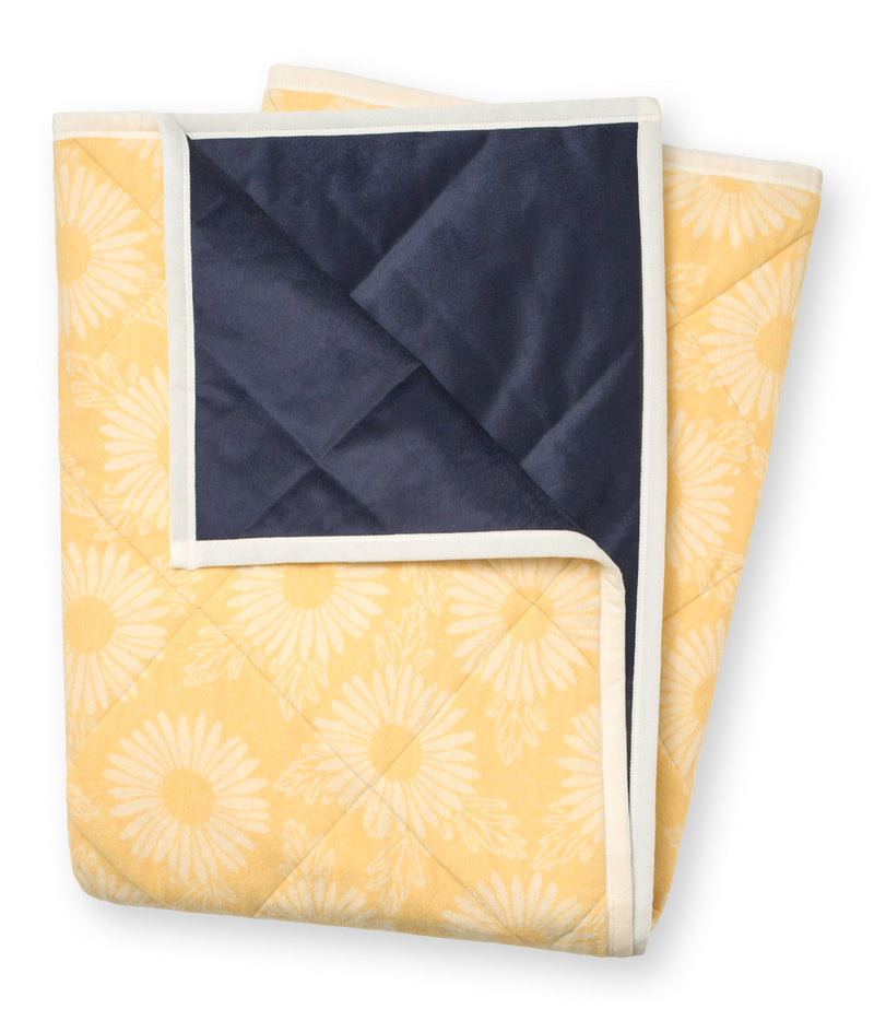 Folded outdoor blanket with yellow daisy pattern on one side and navy blue on the reverse, bordered in cream.