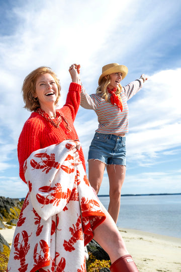 White and red blanket with lobster print worn by woman at beach with ocean and sky in background.4