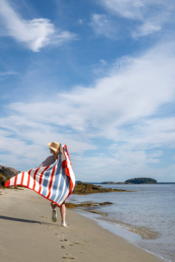 Red and white striped blanket held by person standing on beach facing ocean.5