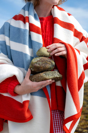 Red and white striped blanket draped over person wearing red sweater, holding rocks outdoors.3