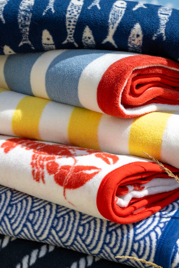 Stacked folded blankets in blue, red, yellow, and white with scallop, stripe, and geometric patterns.4