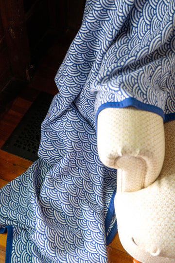 Blue and white scallop-patterned blanket with cream binding draped over a chair.3