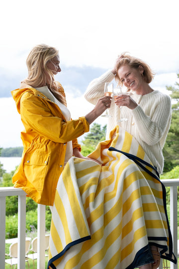 Striped blanket in yellow and white with navy trim draped over a deck railing.2