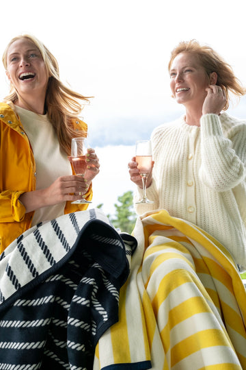 Two women sitting outdoors with striped blankets in yellow and white, and navy and white stripes.3