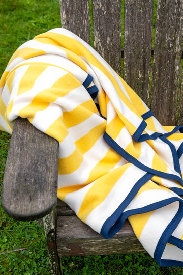 Yellow and white striped blanket with navy binding draped over a wooden chair.5