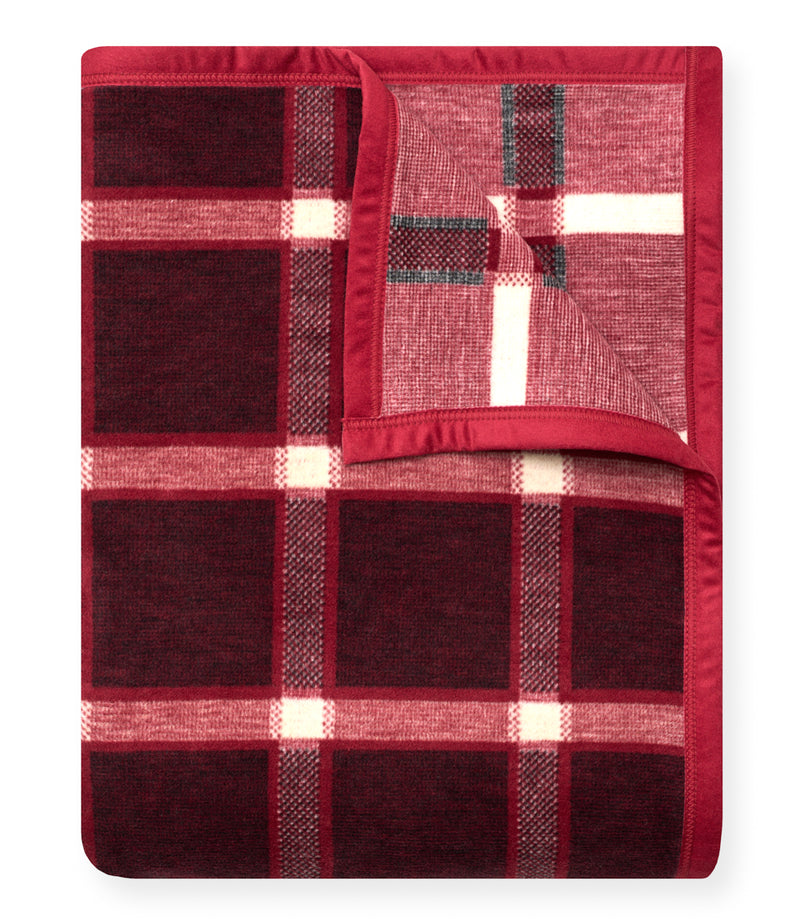 Red and burgundy plaid blanket with cream and charcoal stripes in a large grid pattern, folded with red binding visible along
