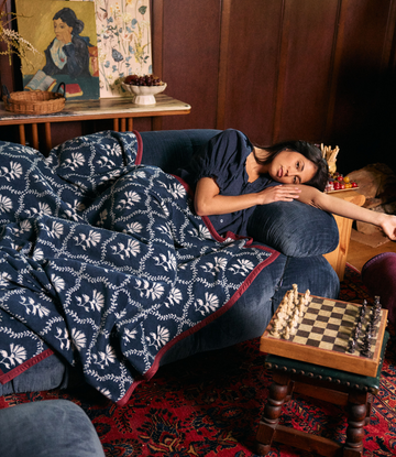 Navy blanket with white floral trellis pattern and burgundy trim draped over couch.2
