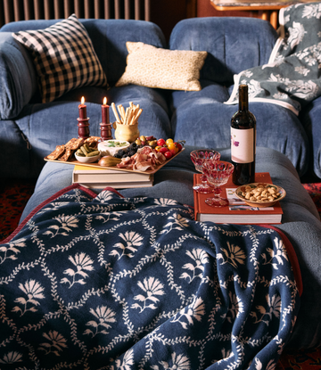 Navy blanket with cream floral and trellis pattern, displayed over blue sofa with red binding.4
