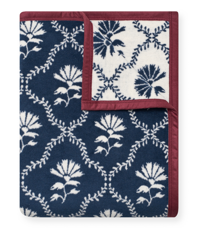 Folded blanket with navy and cream floral trellis pattern, burgundy binding, showing both coordinating print sides.