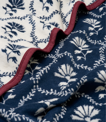 Blanket with navy floral and vine pattern on cream side, burgundy binding, shown folded to display both sides.5