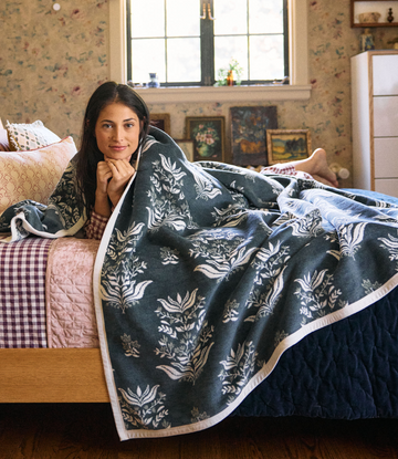 Dark blue blockprint blanket with cream floral motifs and white trim, draped over a bed.3