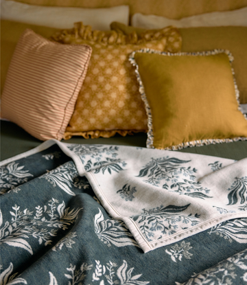 Cream and dark teal blockprint blanket with botanical motif, displayed folded with matching decorative pillows.4