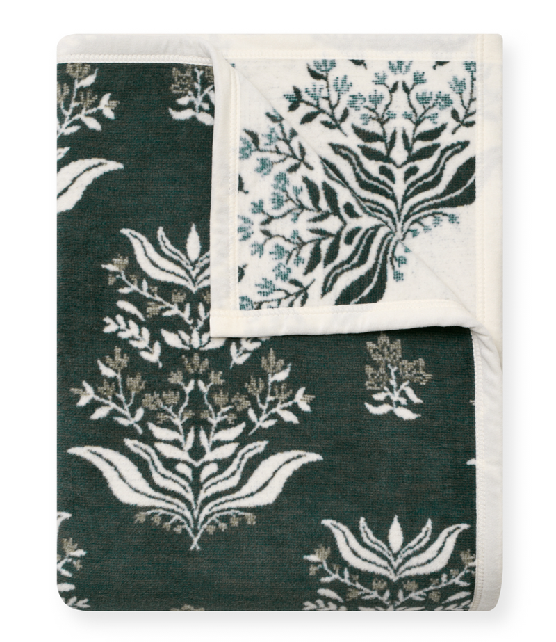 Folded blanket with botanical blockprint design in dark green, cream, and blue tones on both sides.