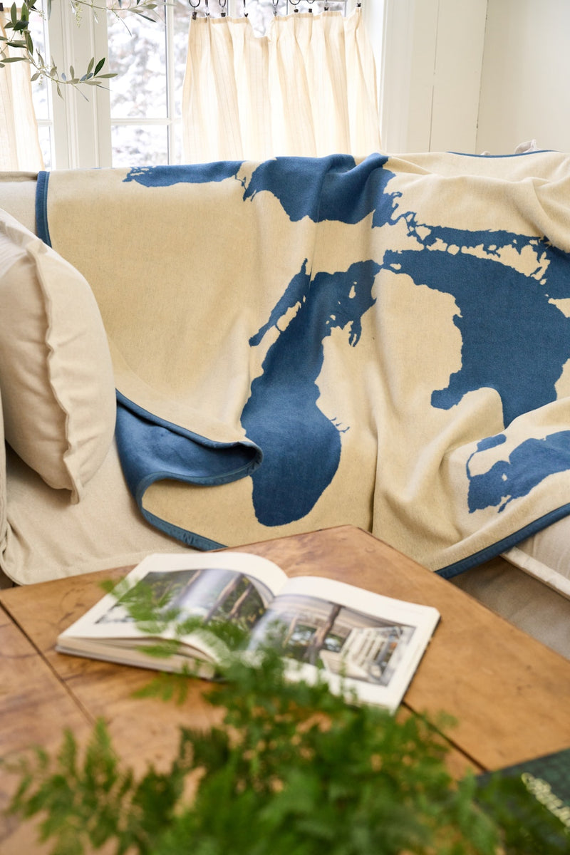 Cream-colored blanket with dark blue Great Lakes map design draped over a couch.