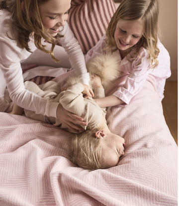 Pink herringbone blanket with two children and one child lying on it.3