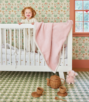 Ballet pink herringbone patterned midi blanket draped over white crib rail.2