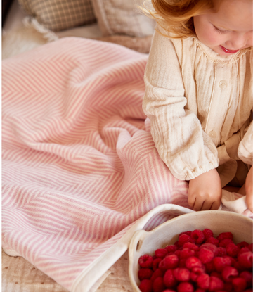 Pink herringbone patterned midi blanket draped over a child's lap during playtime.3