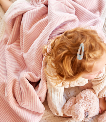 Pink herringbone patterned blanket with gathered folds, draped over a child with reddish-brown hair.4