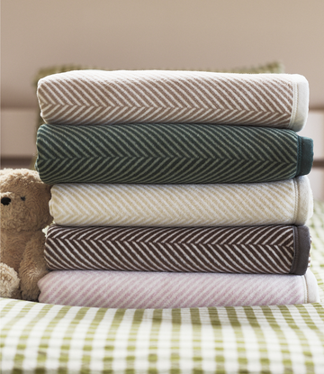 Stack of five folded blankets with herringbone pattern in white, forest green, cream, charcoal, and pink.4