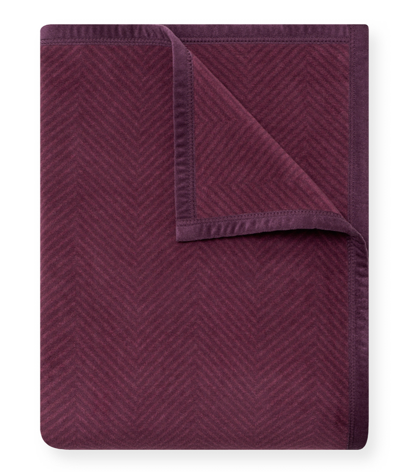 Plum-colored blanket with herringbone texture pattern, folded corner detail visible.