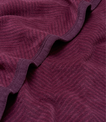 Plum-colored blanket with herringbone weave pattern and stitched binding along folded edges.5
