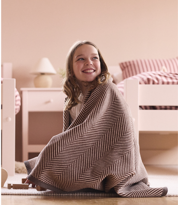 Child wrapped in chocolate brown herringbone patterned blanket sitting on bedroom floor.3