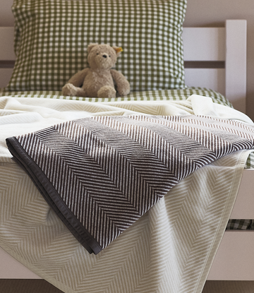 Chocolate brown herringbone patterned blanket draped over a bed with cream and green gingham bedding.4