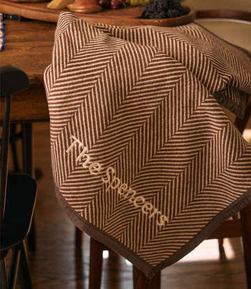 Chocolate brown and cream herringbone patterned blanket with embroidered text draped over a wooden chair.6