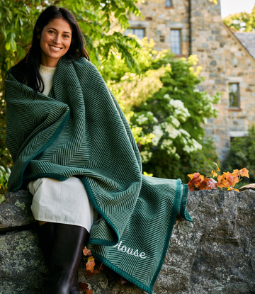 Forest green blanket with white herringbone pattern draped around woman's shoulders outdoors.2