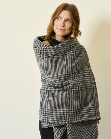 Gray and white plaid shawl with houndstooth pattern worn wrapped around shoulders over black clothing.6