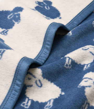 Blue and cream blanket with sheep pattern and blue binding edge, folded to show texture and design.4