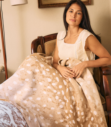 Beige blanket with white deer spot pattern draped over person sitting in wooden chair.4